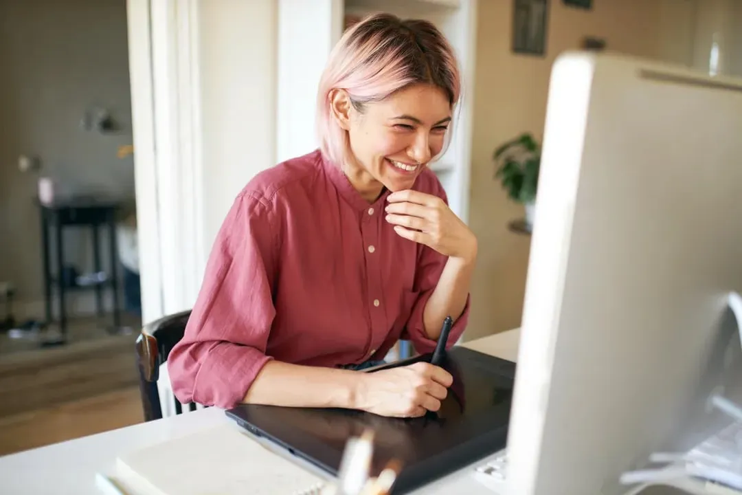 A designer with pink hair laughing as she sketches on a drawing tablet